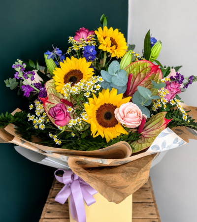 Summer Meadow - Celebrate the beauty of summer with our stunning Summer Meadow bouquet. Handcrafted with radiant sunflowers, elegant roses, delicate daisies, striking anthuriums, blue delphiniums and seasonal blooms, this design captures the relaxed charm of an English summer garden.