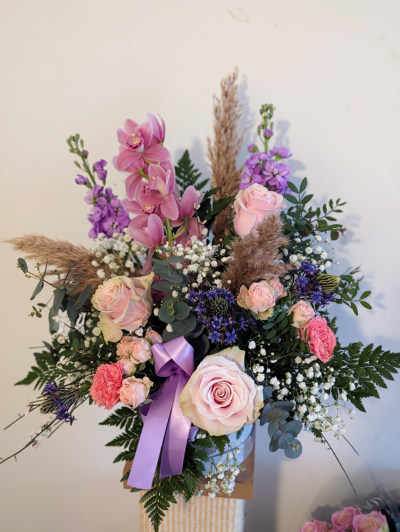 Cherished Love Hatbox - Indulge in elegance with our exquisite Luxury Hatbox Arrangement, designed to impress. Presented in a stylish hatbox, this stunning arrangement features a carefully curated selection of premium blooms, including delicate orchids, sumptuous roses, and other luxurious flowers in soft shades of pink and lilac. Perfect for a special gift, celebration, or simply to add a touch of beauty to any space, this timeless design is both sophisticated and effortlessly chic.