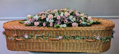 Wicker Casket Spray with Garland – “Dressed Casket” Floral Tribute (Pink & White) - This elegant wicker casket spray is a gentle and timeless tribute, created in soft shades of pink and white. The main spray is designed primarily using premium roses, supported by carefully chosen seasonal flowers and fresh foliage to create a calm and balanced arrangement.

To complete the tribute, a coordinating floral garland dresses the casket, arranged around the sides to complement the natural texture of the wicker. The garland adds depth and continuity, creating a cohesive and thoughtfully finished look.

This casket dressing service offers a softer, more natural alternative to traditional funeral flowers and allows for a more personal farewell. Each tribute is individually designed and made with care and respect.

Colour options:
This design can be created in alternative colour palettes to reflect personal wishes or favourite flowers. Please contact us to discuss bespoke colour choices and seasonal availability.